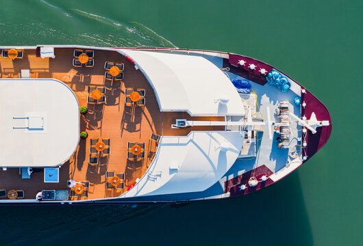 Aerial view of the bow of a river cruise ship sailing on the Rhone River with outdoor tables and seating arranged on the wooden passenger deck in Saulce-sur-Rhone, Auvergne-Rhone-Alpes, France.