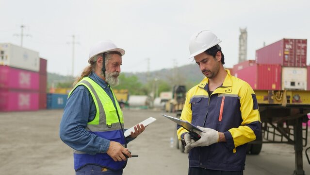 Two logistics workers discuss a shipping manifest on a clipboard in a container yard, collaborating on supply chain management and cargo inspection, reflecting teamwork and modern workplace themes.