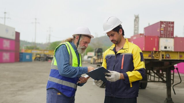 Two logistics workers discuss a shipping manifest on a clipboard in a container yard, collaborating on supply chain management and cargo inspection, reflecting teamwork and modern workplace themes.
