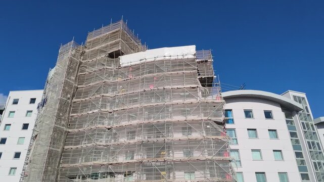 Basingstoke Hampshire England UK. 02.08.2026. Video.  A large building is completely covered in white netting and scaffolding, indicating ongoing construction or repair work on its facade