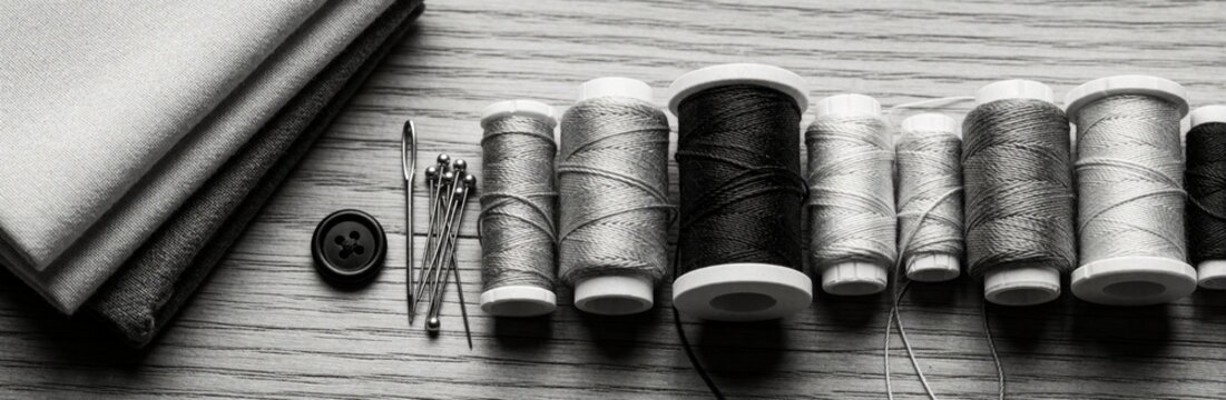 Spools of thread and sewing supplies like fabric and buttons laid on wood. Needlecraft items arranged for sewing, fashion design, or tailoring projects.