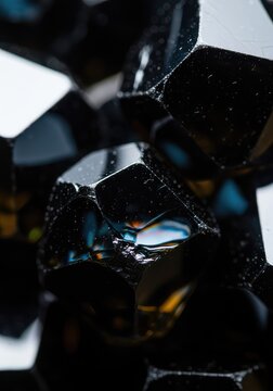 Intricate macro detail of dark, faceted mineral crystals showing sharp geometric edges and reflective obsidian surfaces in an abstract view, faceted, surface, mineral