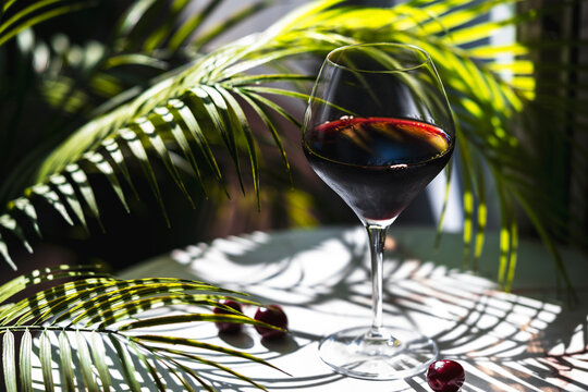 Chilean Carmenere red wine glass with sweet cherries among bright green palm fronds