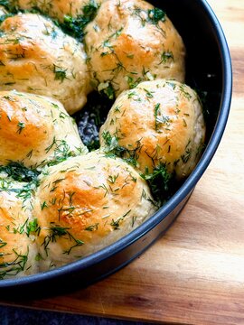 Freshly baked round bread , pampushki, garlic rolls topped with herbs arranged in a black bowl on a wooden cutting board against a dark stone surface