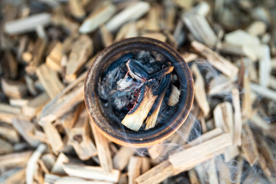 Incense clay pot with burning and smoldering wooden sticks surrounded by Vietnamese cinnamon and agarwood materials in baskets for traditional herbal incense making popular in Vietnam culture.