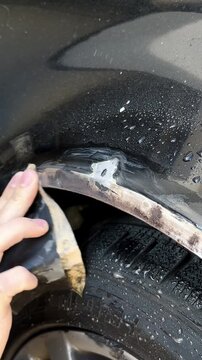 Close-up of a hand using sandpaper to remove rust from a car door trim, showing the gradual cleaning process with visible dirt and moisture on the surface