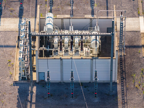 Aerial view of a high voltage power transformer at an electrical substation featuring cooling radiators, fans, and industrial grid infrastructure in Saulce-sur-Rhone, Auvergne-Rhone-Alpes, France.