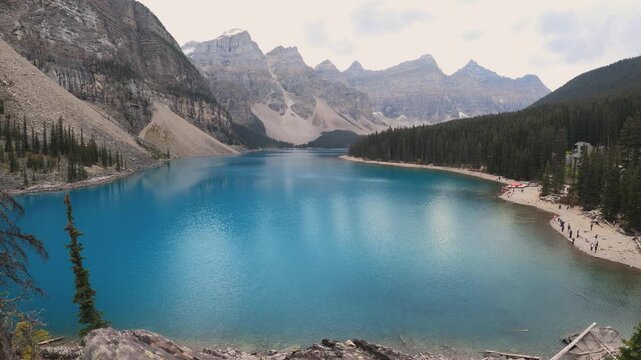 A stunning alpine lake surrounded by dramatic mountain peaks and dense evergreen forests. The crystal-blue Moraine Lake water reflects the peaceful wilderness landscape