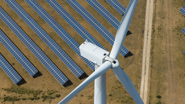 Aerial view of Chelveston Renewable Energy featuring a wind turbine and rows of solar panels in a field in Chelveston, England, United Kingdom.