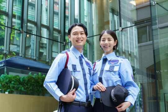 オフィスビルの前に立つ若い日本人男性警備員と女性警備員のポートレート　撮影協力：学校法人電波学園　東京電子専門学校