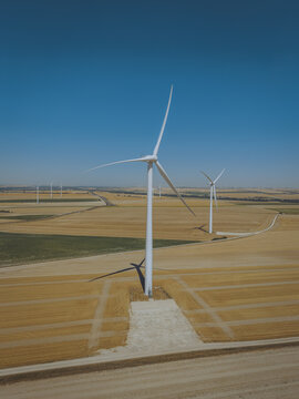 Aerial view of wind turbines standing in a vast golden wheat field under a clear blue sky in Saint-Amand-sur-Fion, Grand Est, France.