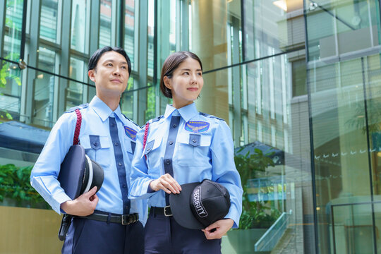 オフィスビルの前に立つ若い日本人男性警備員と女性警備員のポートレート　撮影協力：学校法人電波学園　東京電子専門学校