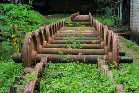 Row of Vintage Train Wheelsets and Axles Lined Up Outdoors with Greenery