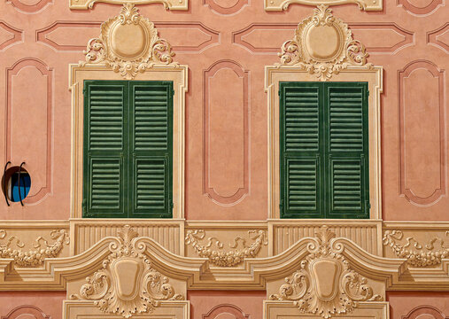 Symmetrical pattern of traditional Ligurian trompe l oeil painted windows on a pink facade in Genoa, Liguria, Italy