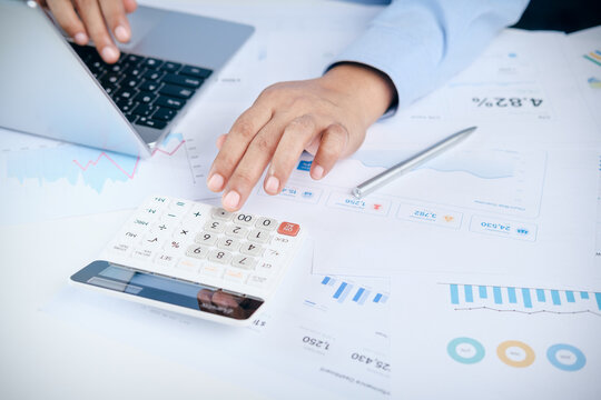 Businessman using calculator and laptop for financial calculation with data analysis charts and reports on office desk, concept of accounting, business budget planning, and investment analysis.