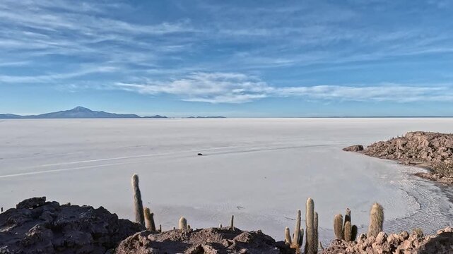 Car crossing the surreal and immense salar de uyuni salt flat in bolivia, seen from isla incahuasi, famous for its giant cacti. Uyuni salt flats, bolivia