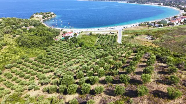 Aerial view of Toroni in Sithonia, Halkidiki, Greece, showing a busy Mediterranean beach with turquoise crystal-clear water, swimmers, sunbeds and beachfront hotels on a sunny summer day.