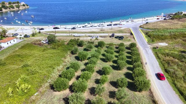 Aerial view of Toroni in Sithonia, Halkidiki, Greece, showing a busy Mediterranean beach with turquoise crystal-clear water, swimmers, sunbeds and beachfront hotels on a sunny summer day.
