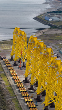 Aerial view of yellow wind turbine jacket foundations lined up at an industrial port facility in Edinburgh, Scotland, United Kingdom.