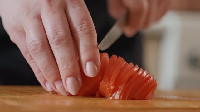 Closeup view of hands slicing raw salmon into thin, uniform sashimi pieces on wooden cutting board, showing careful knife movement, steady fingers, fresh texture, and focused food preparation
