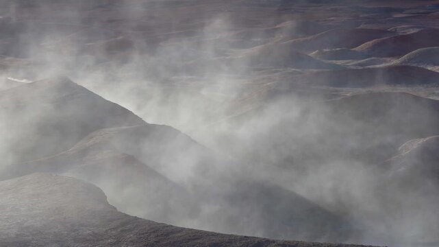 Geothermal steam and vapor rising from fumaroles and vents in a dramatic, surreal volcanic landscape. Eerie and desolate scenery in morning light. Polques hot springs. Atacama desert