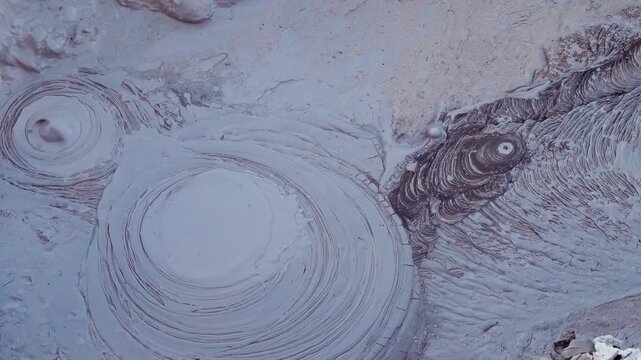Bubbling mud pots boiling in a geothermal field. Close up view of the volcanic activity and natural texture with rising steam and gases. Polques hot springs