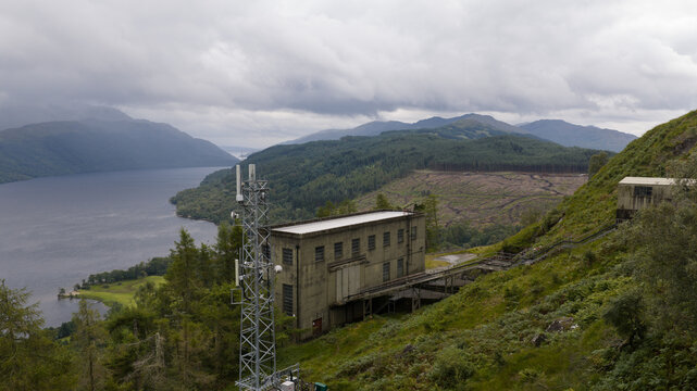 Aerial view of the Loch Sloy power station and telecommunications tower near the lake, surrounded by forested hills and cloudy sky in Argyll and Bute Council, Scotland, United Kingdom.