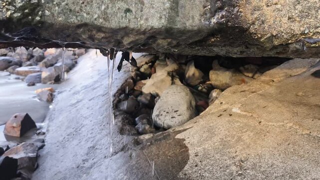 Water dripping from coastal rock on a rocky beach with crashing ocean waves, concept of coastal erosion, climate change, and sea level rise.