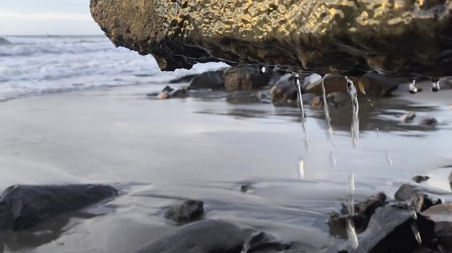 Water dripping from coastal rock on a rocky beach with crashing ocean waves, concept of coastal erosion, climate change, and sea level rise.