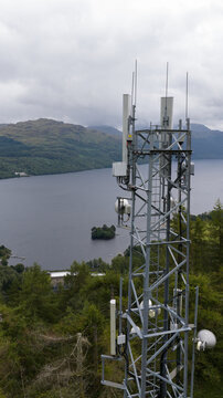 Aerial view of a telecommunications tower overlooking Loch Sloy, surrounded by lush green trees and hills under a cloudy sky in Argyll and Bute Council, Scotland, United Kingdom.