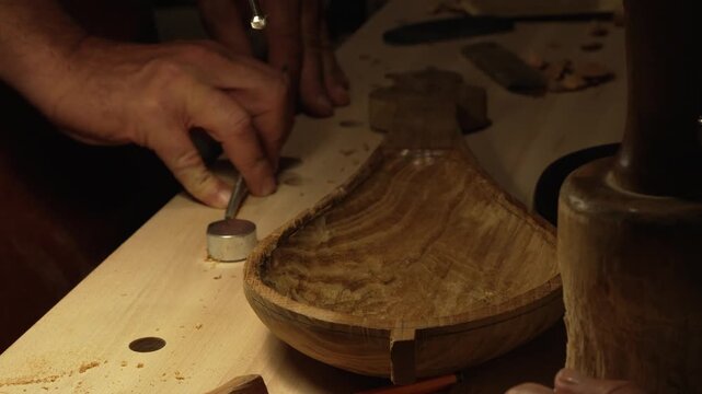 The master crafts traditional wooden string instruments by hand. The traditional musical instrument is the Calabrian lyre. The master works in the cozy light of his workbench.