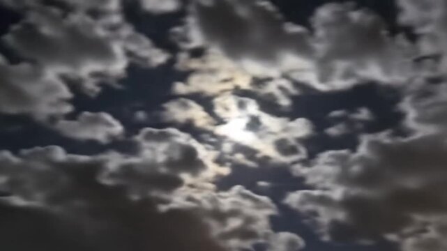Full moon glowing behind moving dark clouds in the night sky