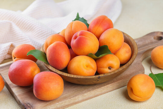 Close up of fresh ripe apricots in rustic wooden bowl with green leaves on yellow textured background. Healthy seasonal summer fruit, healthy food, nutrition, ingredient for cooking and desserts