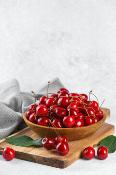 Fresh ripe sweet cherries in wooden bowl on rustic cutting board with green leaves and linen cloth on white textured background. Healthy summer fruit, red berries, fresh seasonal harvest, healthy food