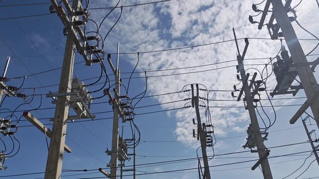Pan right video of automatic circuit and electrical power distribution equipment on concrete poles under dramatic cloudy sky with bright sunlight.