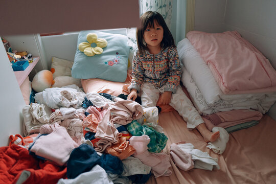 Child Sitting in Messy Room With Clothes Scattered Around
