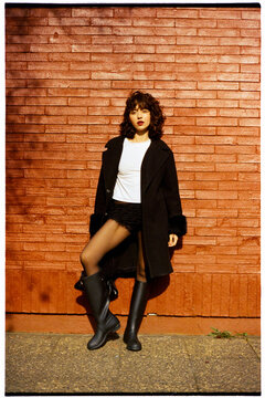 Young woman posing by brick wall