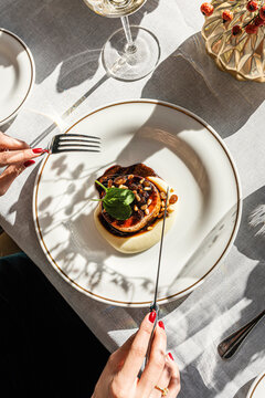 Hands holding cutlery eating a gourmet meat dish at a restaurant
