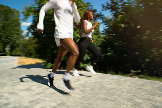 Black runners man and woman blurred into motion at summer street.