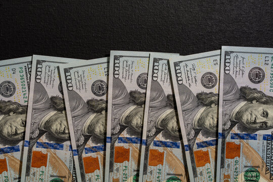One hundred US dollar bills row on black background. Closeup overhead shot of several one hundred dollar banknotes arranged in row on dark black textured background with copy space