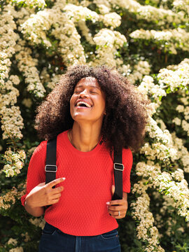 Happy Black Woman Laughing Outdoors With Backpack Among Flowers