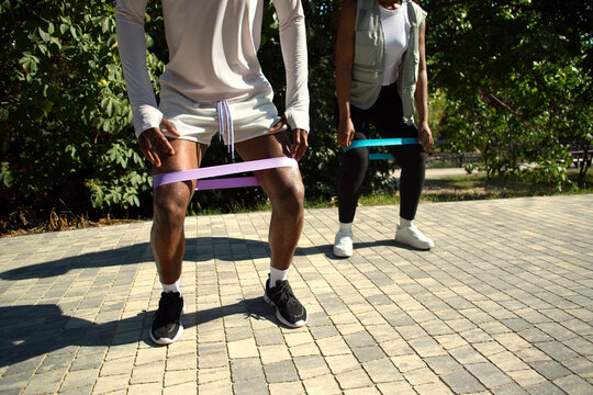Two Black runners using resistance bands for leg workout outdoors.
