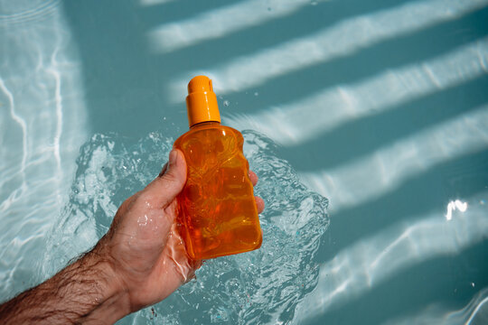 Holding Sunscreen Above Swimming Pool Water