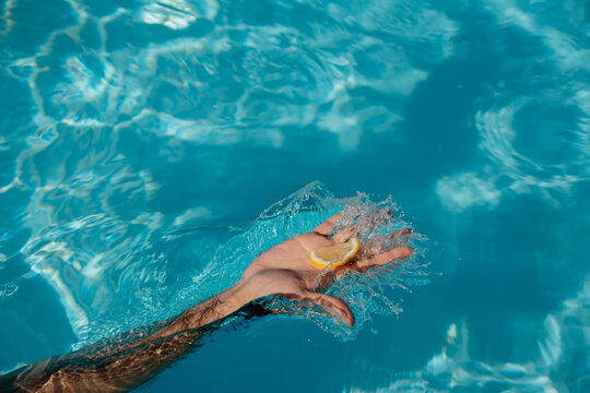 Hand Splashing Pool Water With Lemon Slice