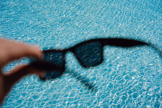 Holding Sunglasses Above Clear Swimming Pool Water
