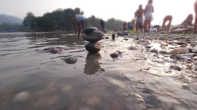 Defocused Sacred River Bathing at Devghat Dham, Nepal, with Balanced River Stones in Foreground, Hindu Pilgrimage, Spiritual Ritual, Peaceful Riverside Landscape and Cultural Heritage