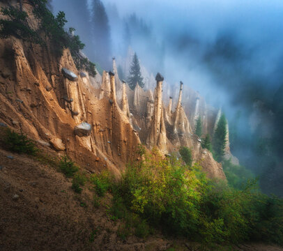 Earth pyramids of Platten geological rock formations in fog in Dolomites, Italy. Alpine natural erosion landscape with soil pillars, balanced stones, pine trees and fog mist on mountain slope. Autumn