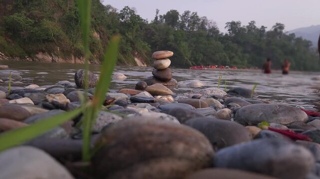 Defocused Sacred River Bathing at Devghat Dham, Nepal, with Balanced River Stones in Foreground, Hindu Pilgrimage, Spiritual Ritual, Peaceful Riverside Landscape and Cultural Heritage