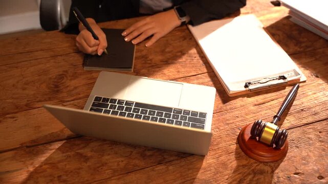 Desk Setup for Legal Professional: A focused lawyer works diligently at their wooden desk, surrounded by legal documents, a laptop, and a gavel, symbolizing justice and decision-making.