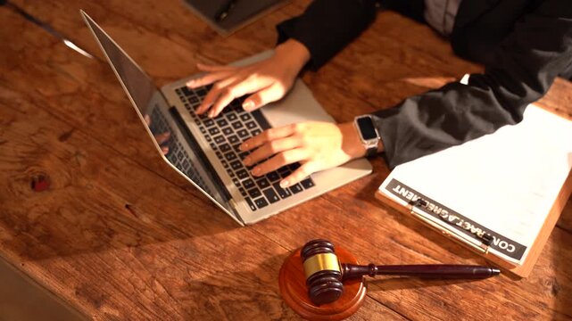 Legal Professional at Work: A lawyer or legal professional's hands typing on a laptop keyboard, with a gavel and legal documents on a wooden desk, signifying diligent legal work and justice.